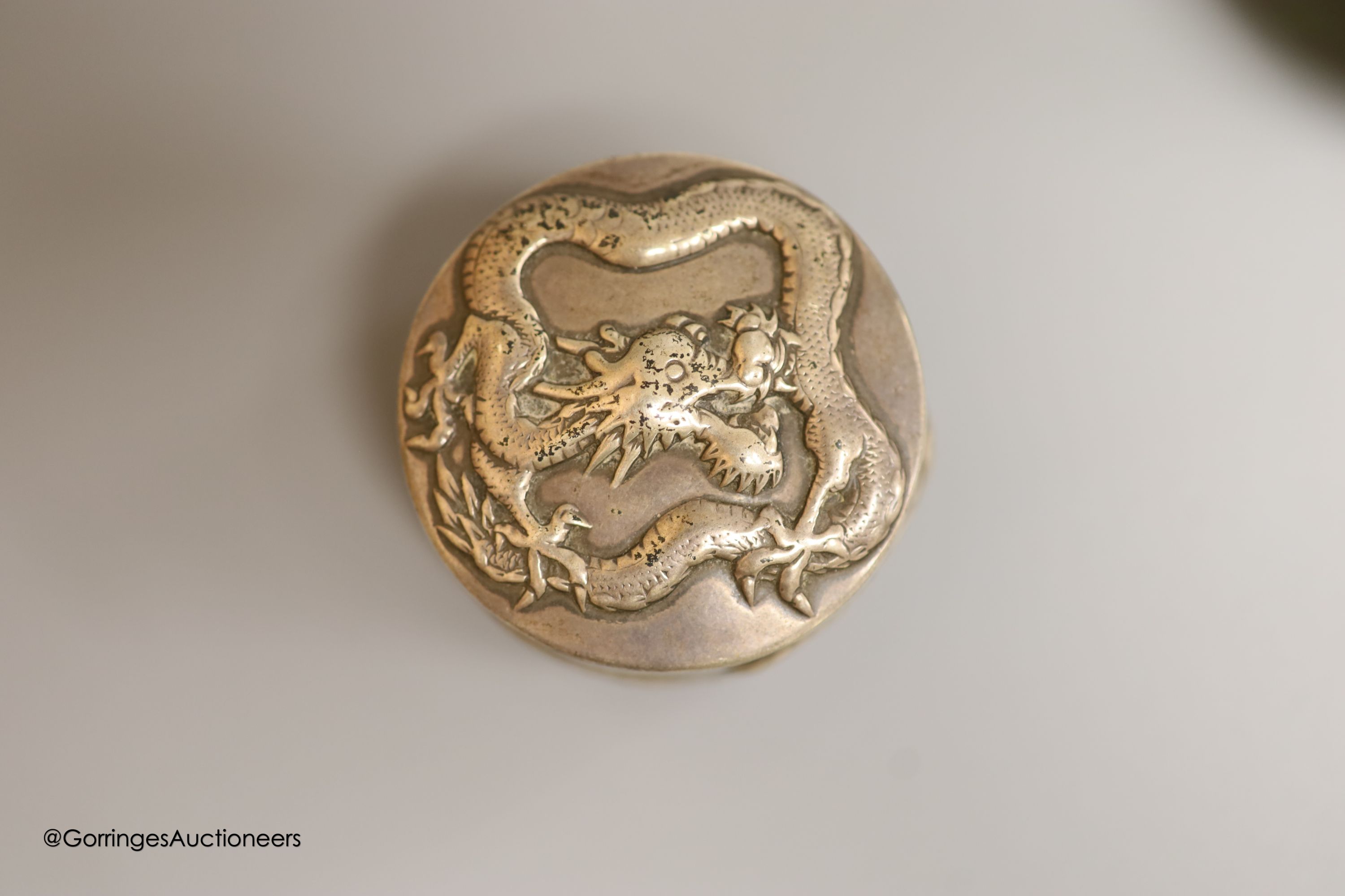 A late 19th/early 20th century Chinese Export white metal circular box, by Wang Hing, embossed with dragons, diameter 5cm, together with a similar white metal overlaid green glass scent flask by Wang Hing, height 11.6cm.